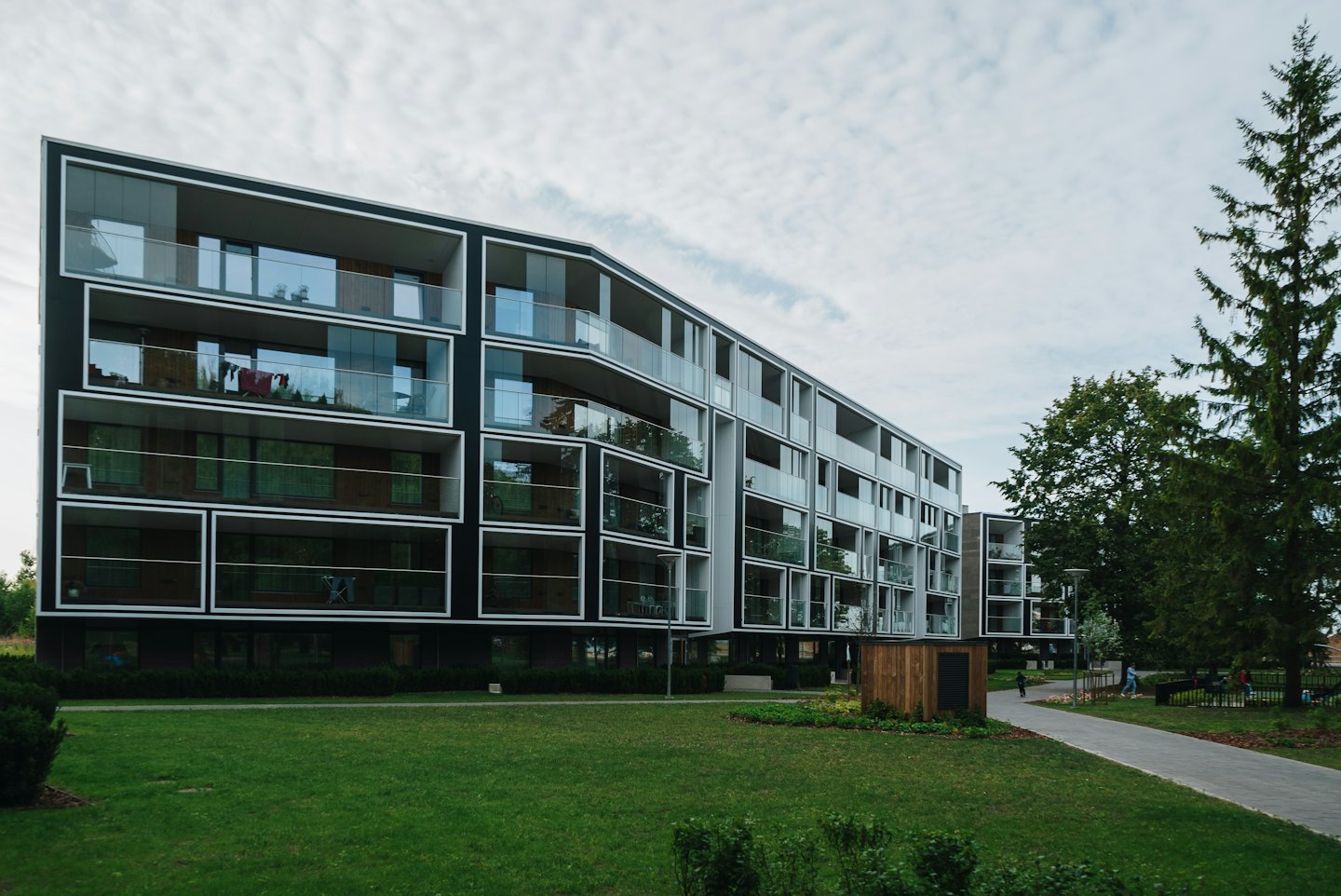 Modern apartment building with glass balconies surrounded by green grass.