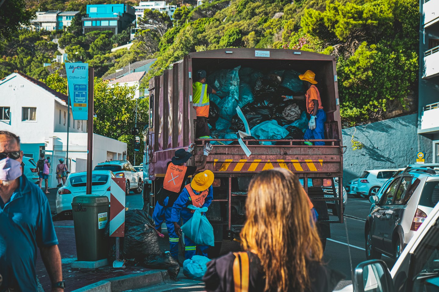 Sanitation workers loading trash bags into a garbage truck on a sunny street.