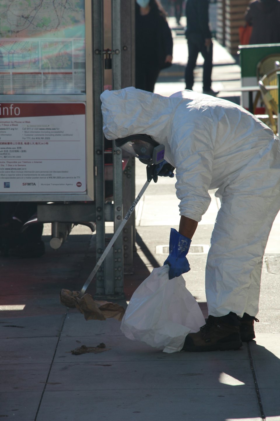 A professional in a hazmat suit cleans trash from a sidewalk.