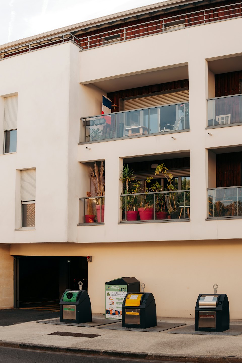 Modern apartment building with a French flag and sidewalk recycling bins.